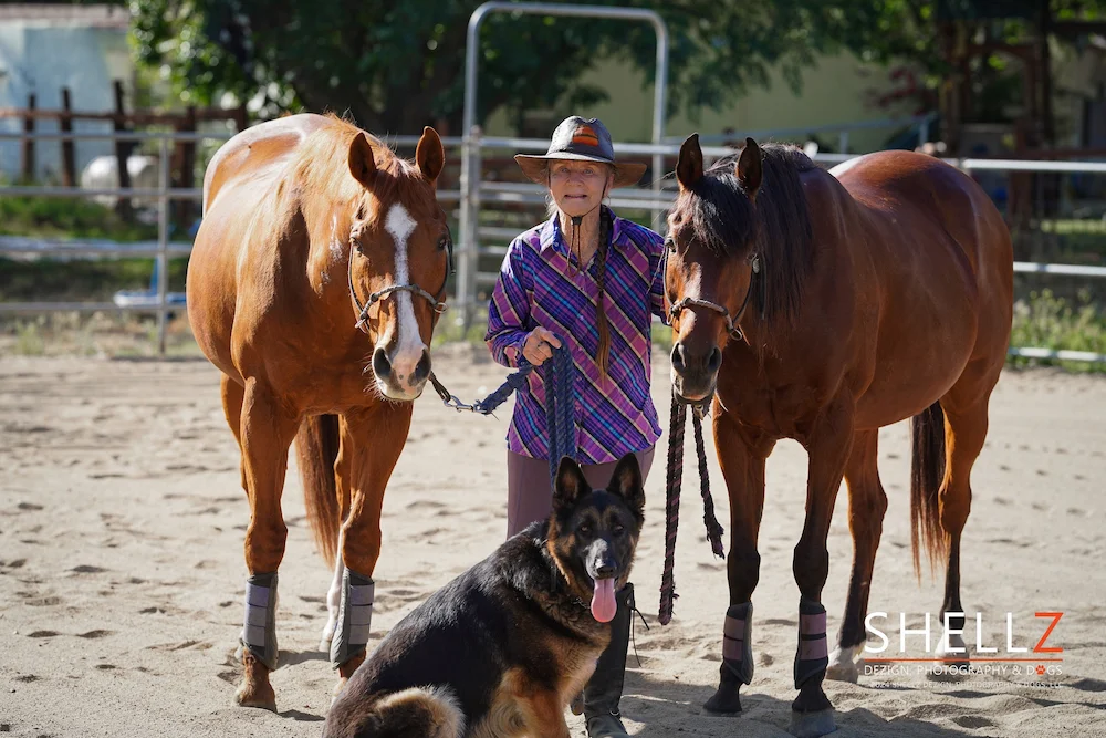 An SDCE resident with two horses and a German Shepherd in a Ramona equestrian arena, capturing the everyday horse culture of San Diego Country Estates